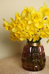 Beautiful daffodils in vase on wicker table near light wall