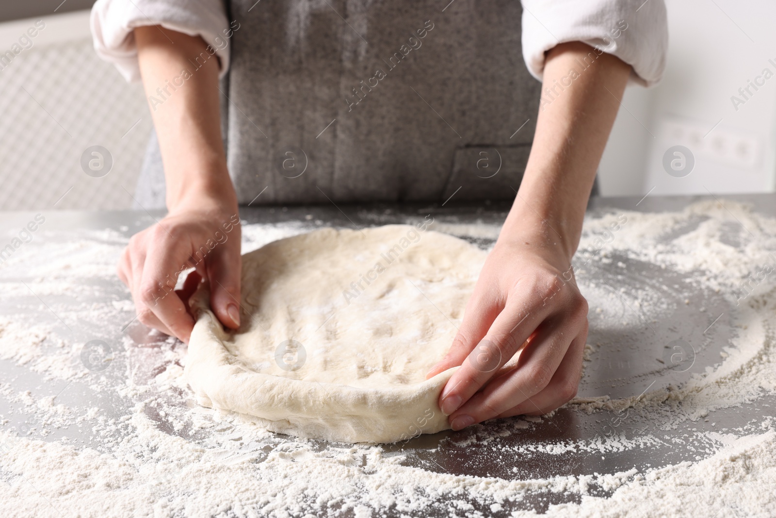 Photo of Woman kneading dough at table in kitchen, closeup