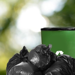 Plastic bags full of garbage and waste bin on blurred background, space for text