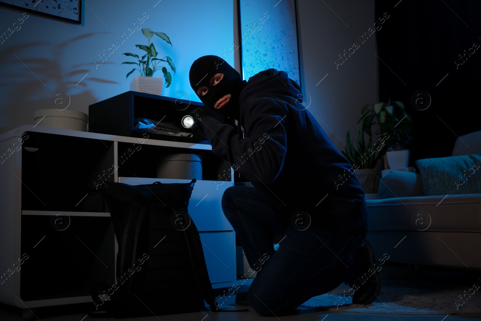 Photo of Thief with flashlight near steel safe indoors at night