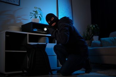 Thief with flashlight near steel safe indoors at night