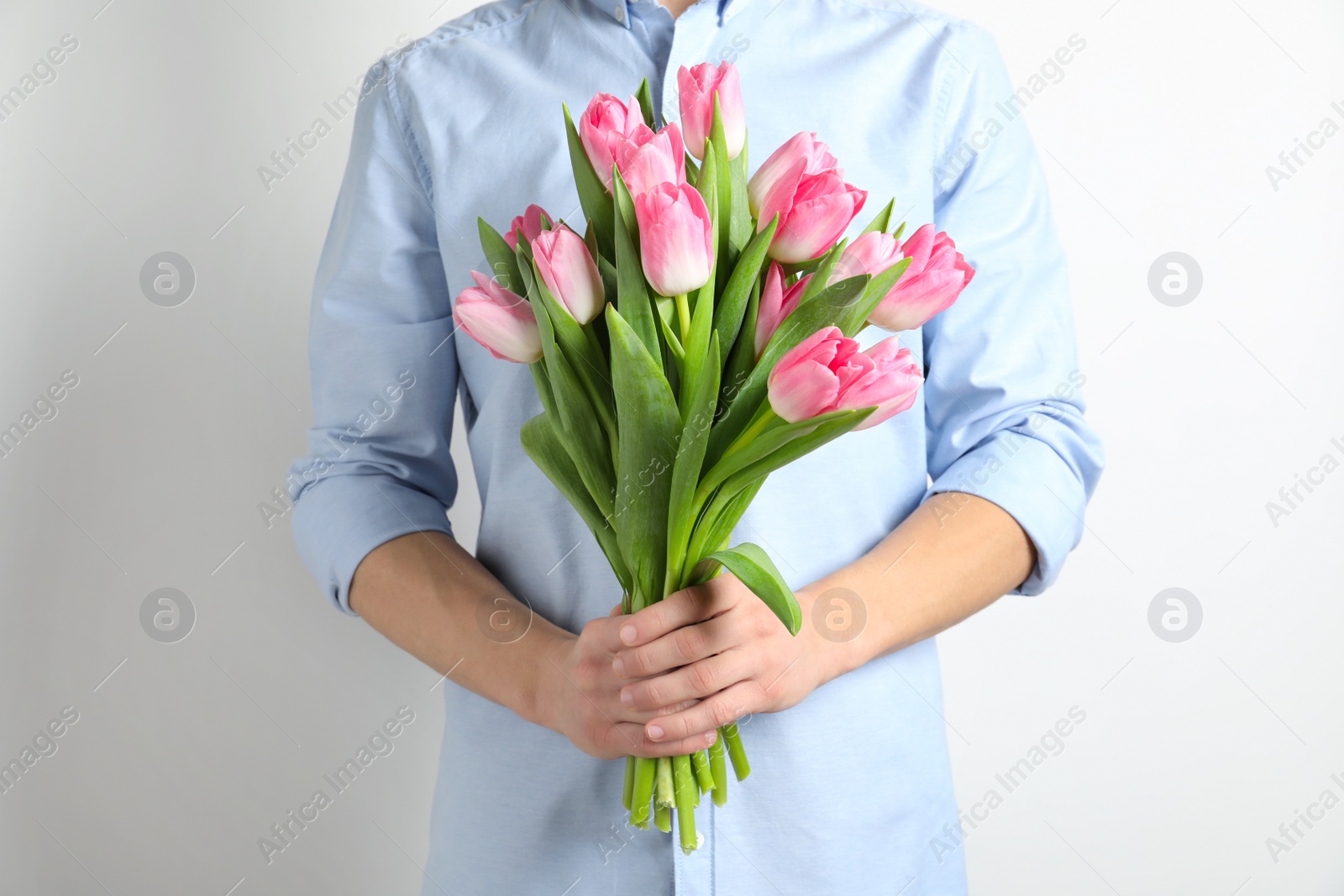 Photo of Man holding bouquet of beautiful spring tulips on light background, closeup. International Women's Day