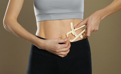 Photo of Young woman measuring body fat with caliper on beige background, closeup