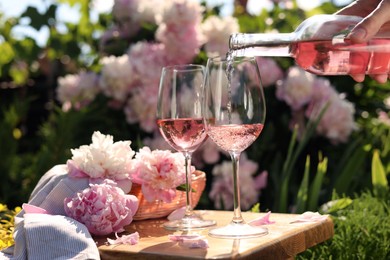 Woman pouring rose wine into glass at table in garden, closeup