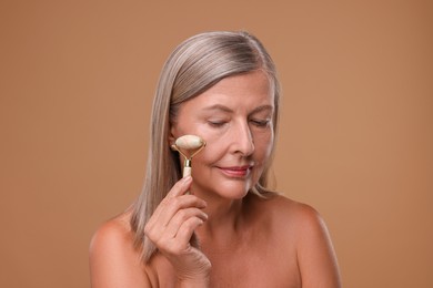 Photo of Woman massaging her face with jade roller on brown background