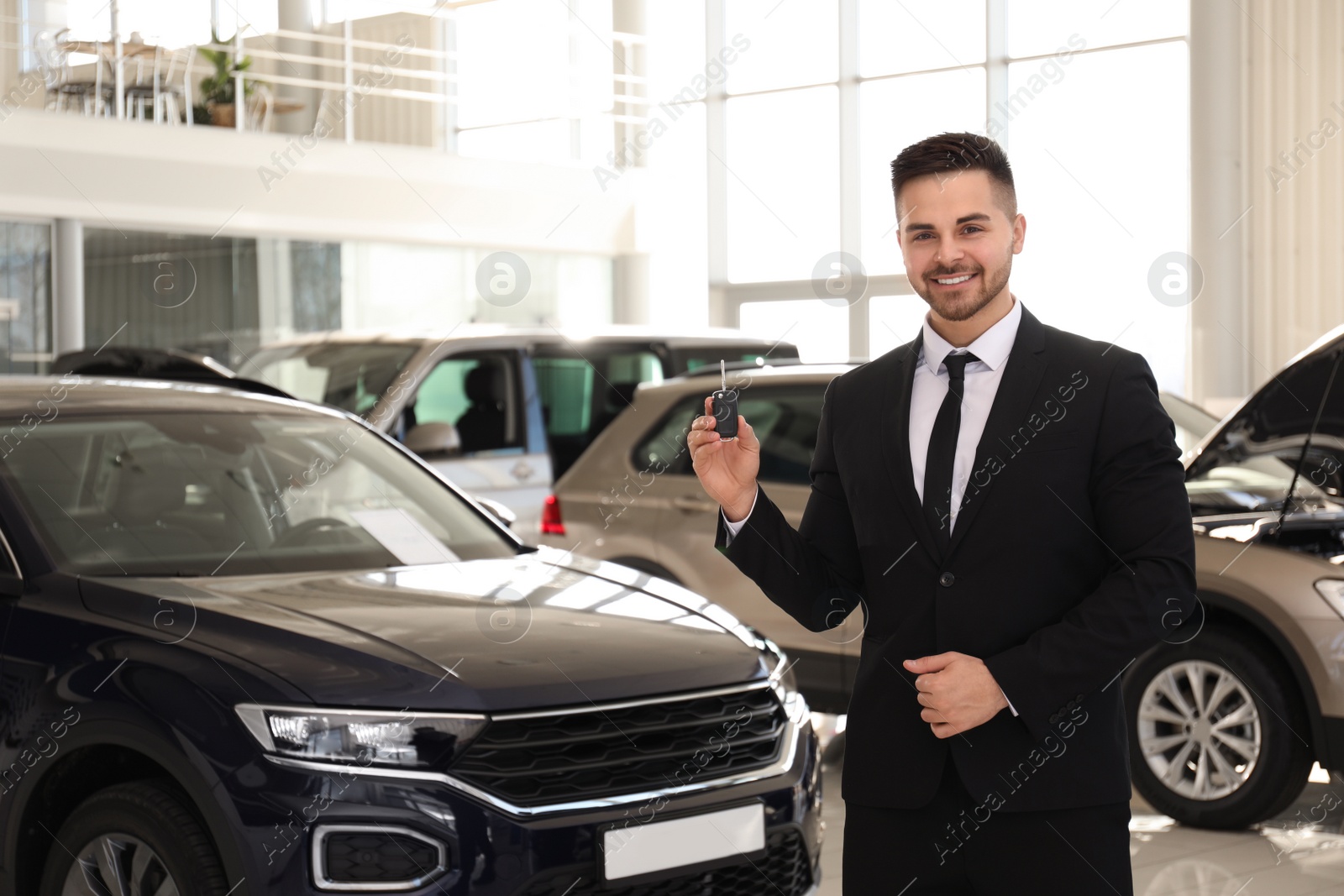 Photo of Salesman with key in modern car salon