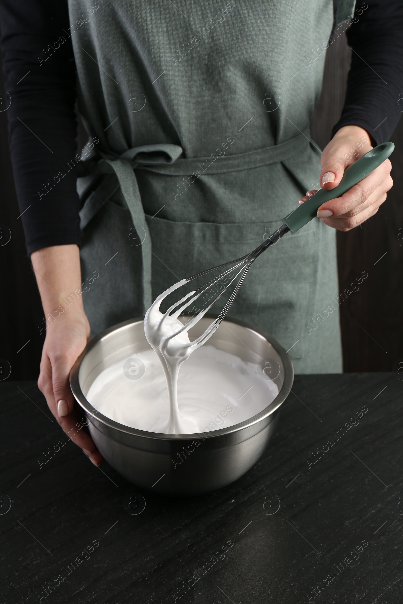 Photo of Woman making whipped cream with whisk at black table, closeup