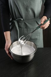 Woman making whipped cream with whisk at black table, closeup