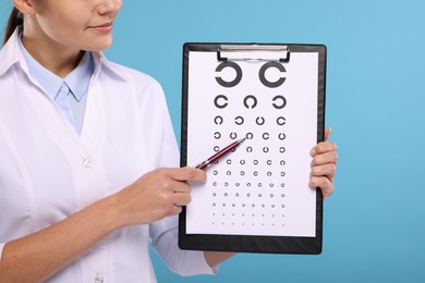 Photo of Ophthalmologist pointing at vision test chart on light blue background, closeup