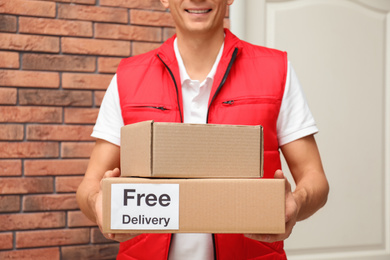 Courier holding parcels with sticker Free Delivery indoors, closeup