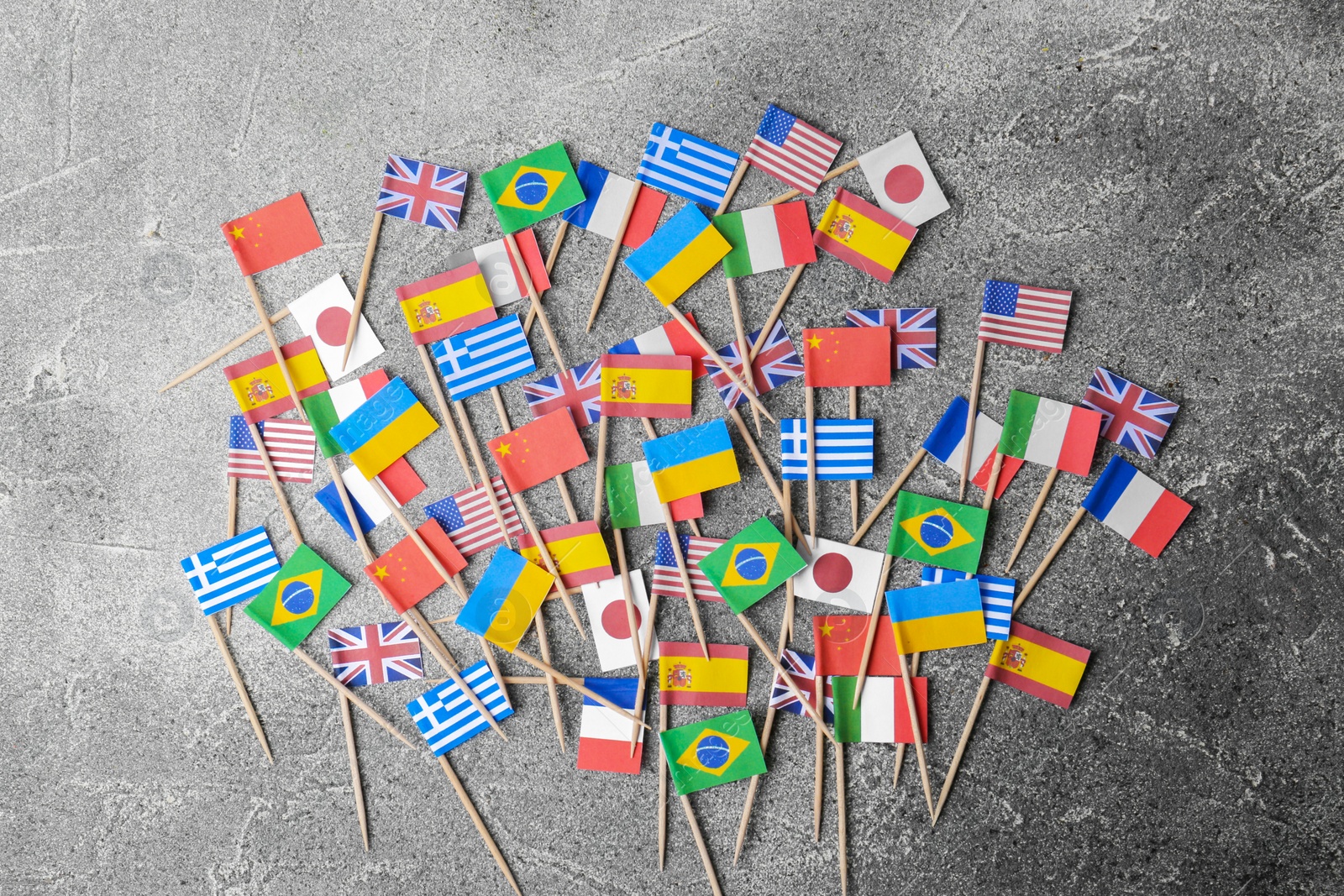 Photo of Many small paper flags of different countries on grey table, flat lay