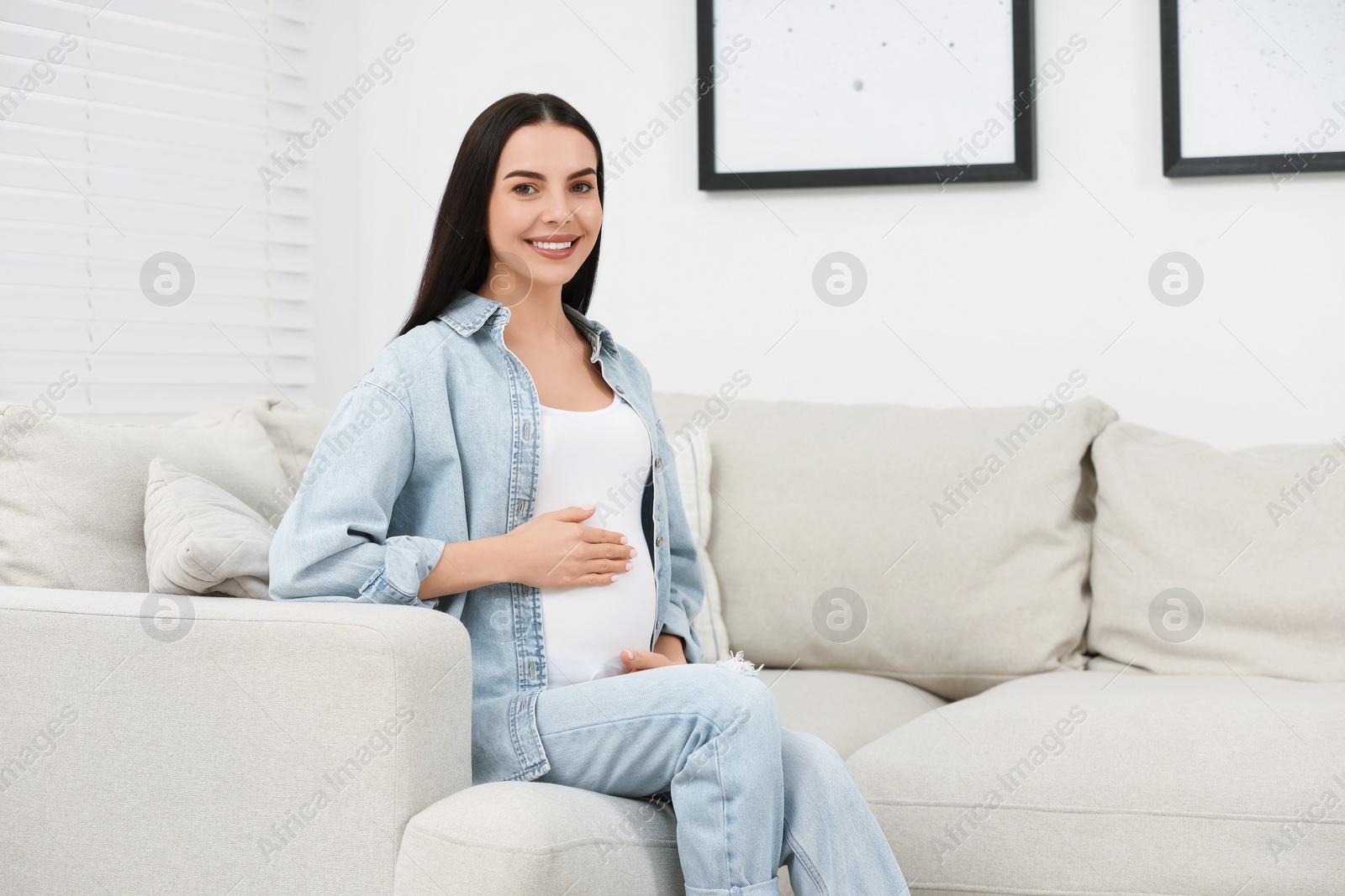 Photo of Happy pregnant woman on sofa at home, space for text