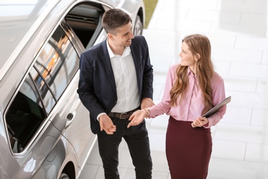 Young saleswoman working with client in car dealership