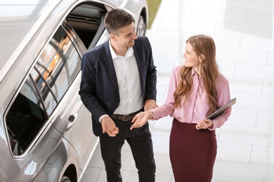 Photo of Young saleswoman working with client in car dealership