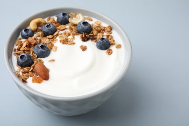 Photo of Bowl with yogurt, blueberries and granola on light grey background, closeup. Space for text