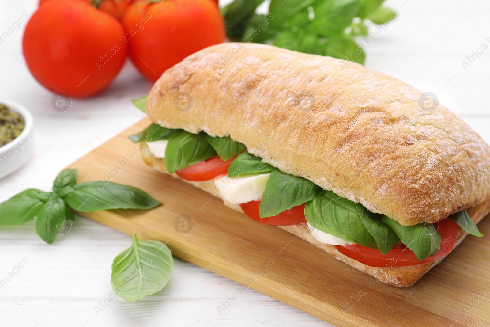 Photo of Delicious Caprese sandwich with mozzarella, tomatoes and basil on white wooden table, closeup