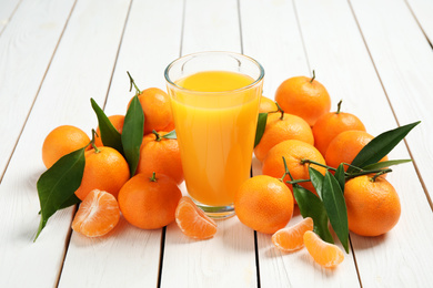 Glass of fresh tangerine juice and fruits on white wooden table