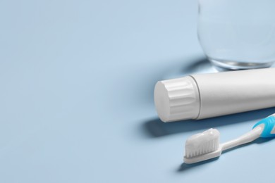 Photo of Plastic toothbrush with paste and glass of water on light background, space for text