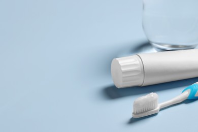 Plastic toothbrush with paste and glass of water on light background, space for text