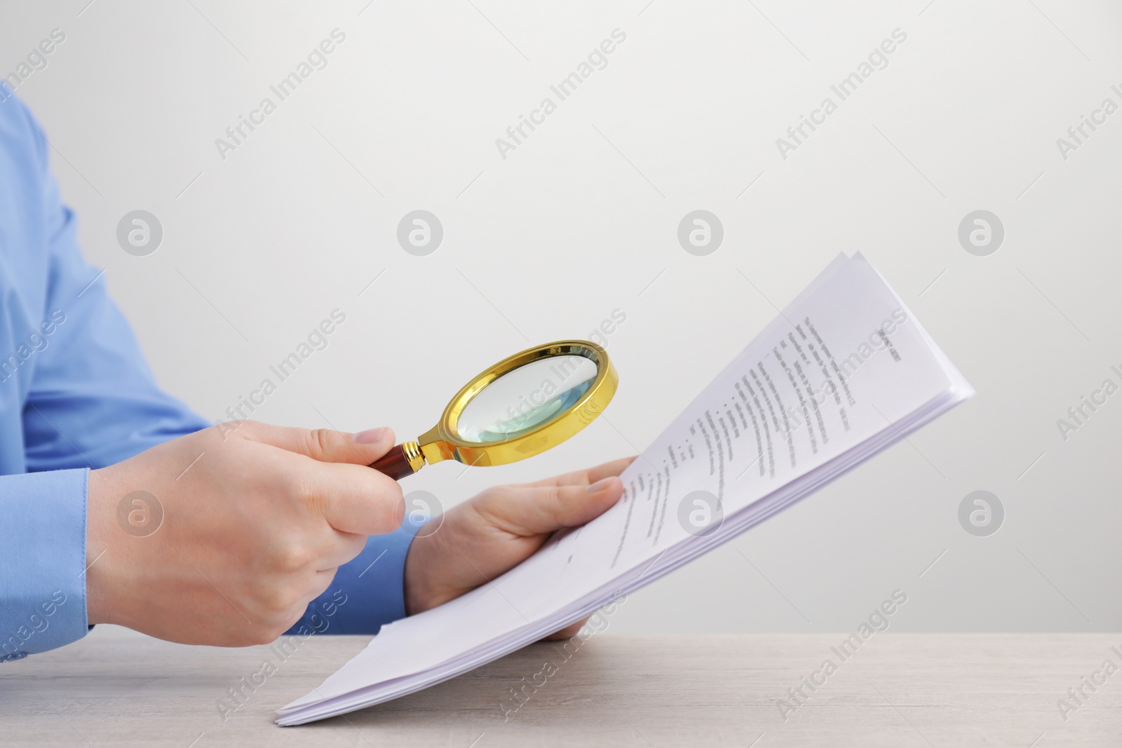 Photo of Man looking at document through magnifier at white wooden table, closeup. Searching concept