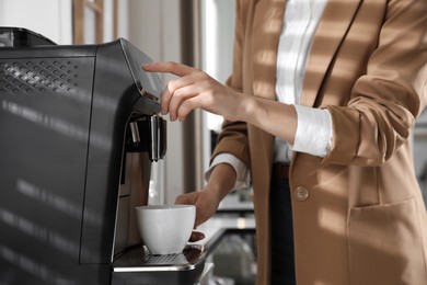 Young woman preparing fresh aromatic coffee with modern machine in office, closeup