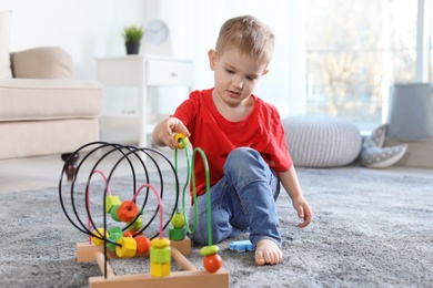 Cute child playing with bead maze on floor indoors