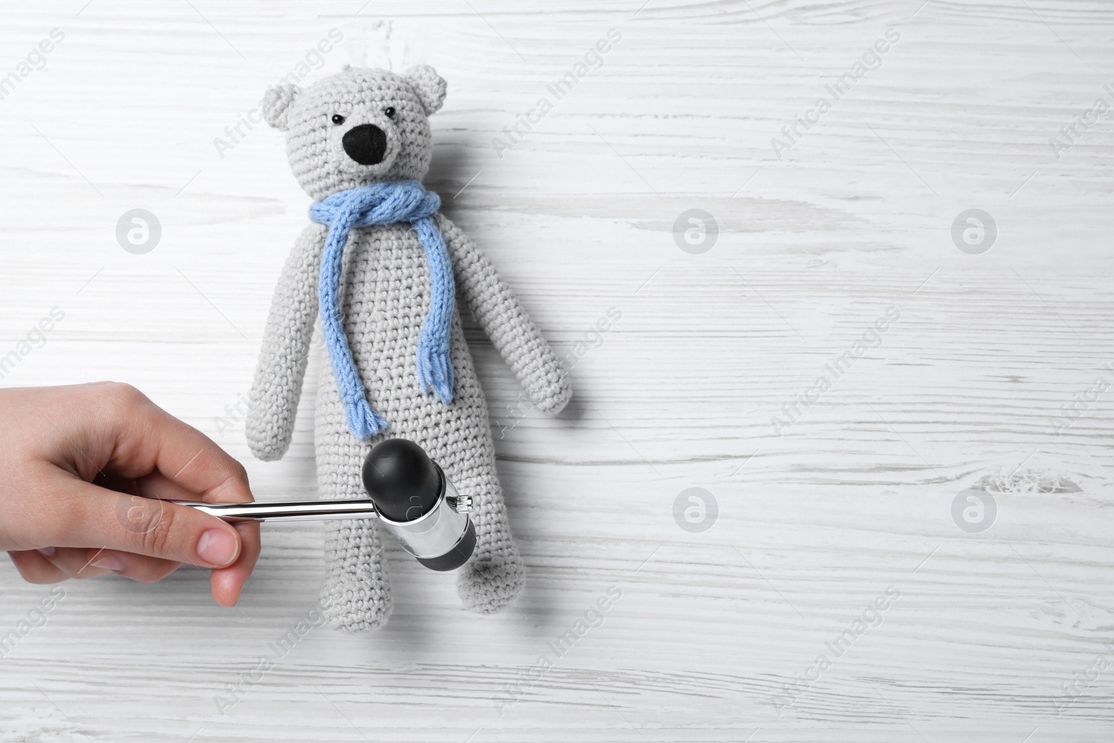 Photo of Woman pretending to test teddy bear's reflexes with hammer on white wooden background, top view and space for text. Nervous system diagnostic