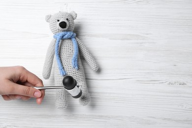 Photo of Woman pretending to test teddy bear's reflexes with hammer on white wooden background, top view and space for text. Nervous system diagnostic