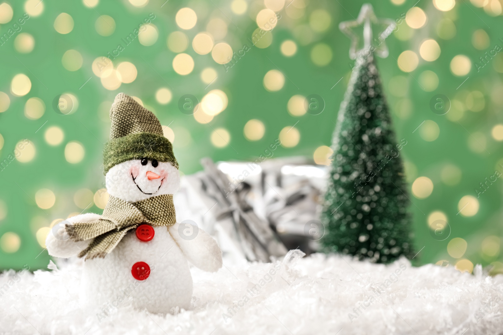 Photo of Snowman toy on snow against blurred festive lights, space for text. Christmas decoration