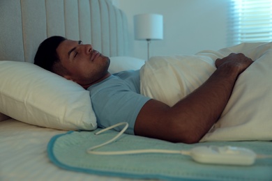 Photo of Man sleeping on electric heating pad in bed at night