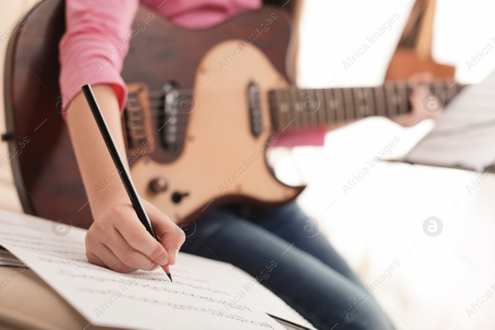 Photo of Little girl with guitar writing music notes indoors, closeup