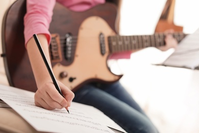 Photo of Little girl with guitar writing music notes indoors, closeup