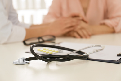 Closeup view of doctor holding senior patient's hands in office, focus on stethoscope