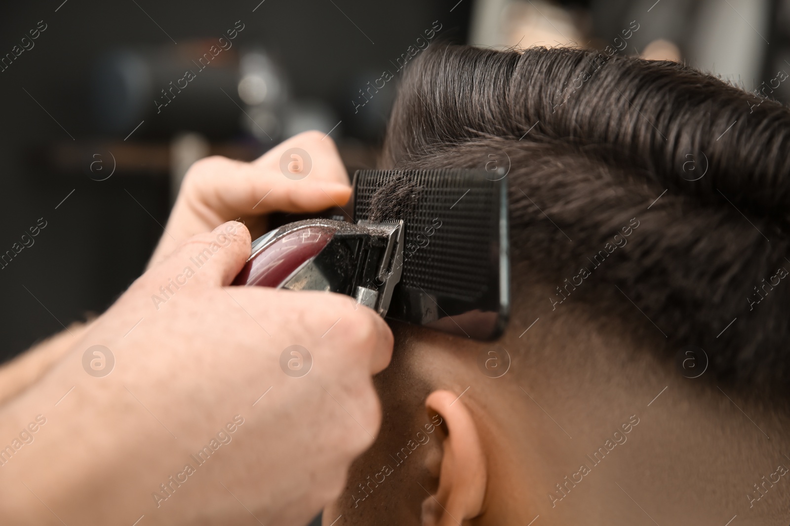 Photo of Professional barber making stylish haircut in salon, closeup