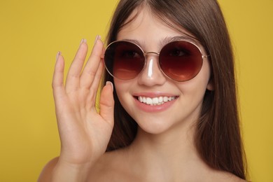 Photo of Teenage girl with sun protection cream on her face against yellow background, closeup