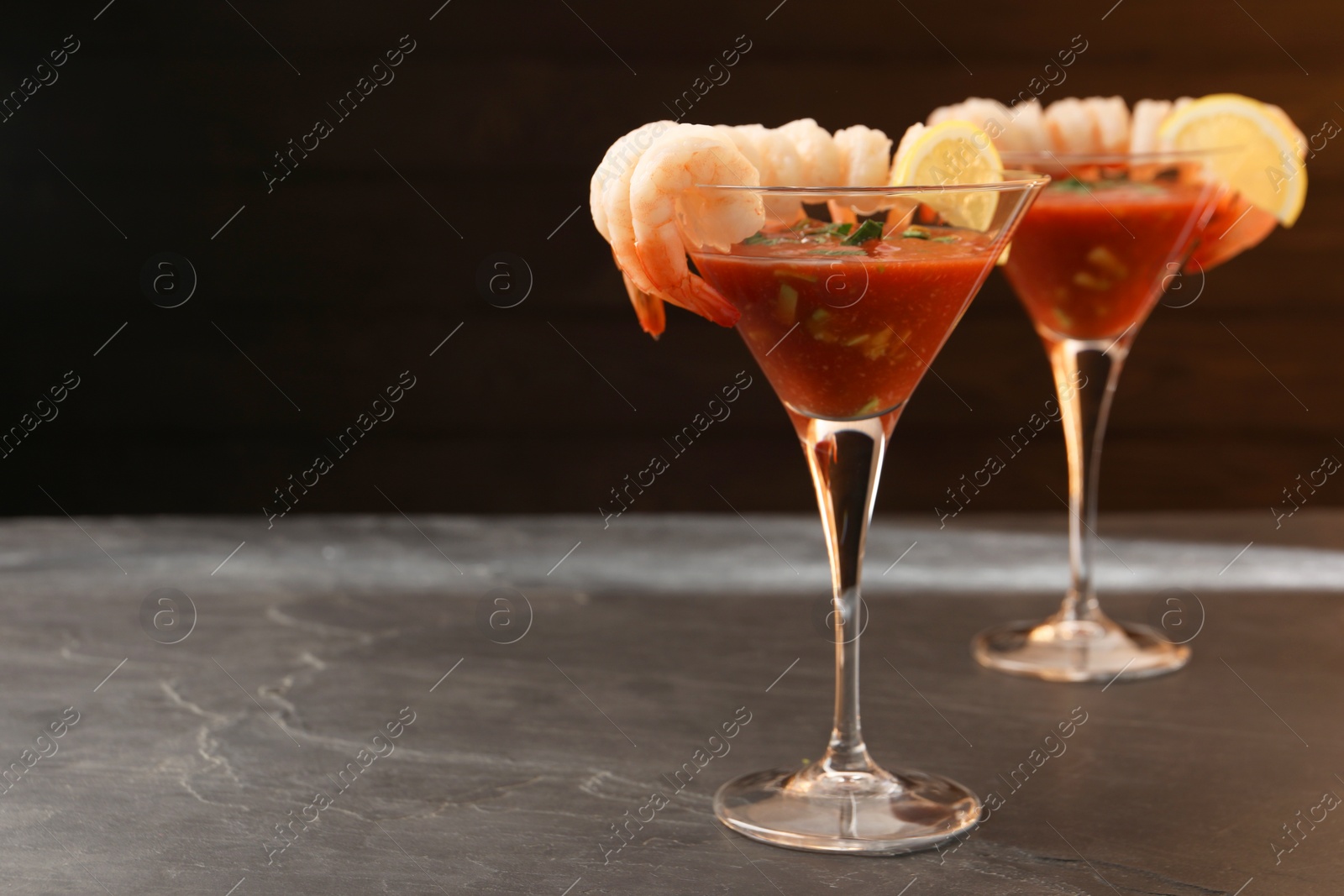 Photo of Tasty shrimp cocktail with sauce in glasses and lemon on grey textured table, space for text