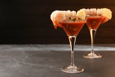 Tasty shrimp cocktail with sauce in glasses and lemon on grey textured table, space for text