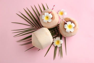 Photo of Fresh coconuts with drinking straws and flowers on pink background, flat lay