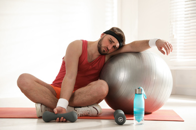 Photo of Lazy young man with sport equipment indoors