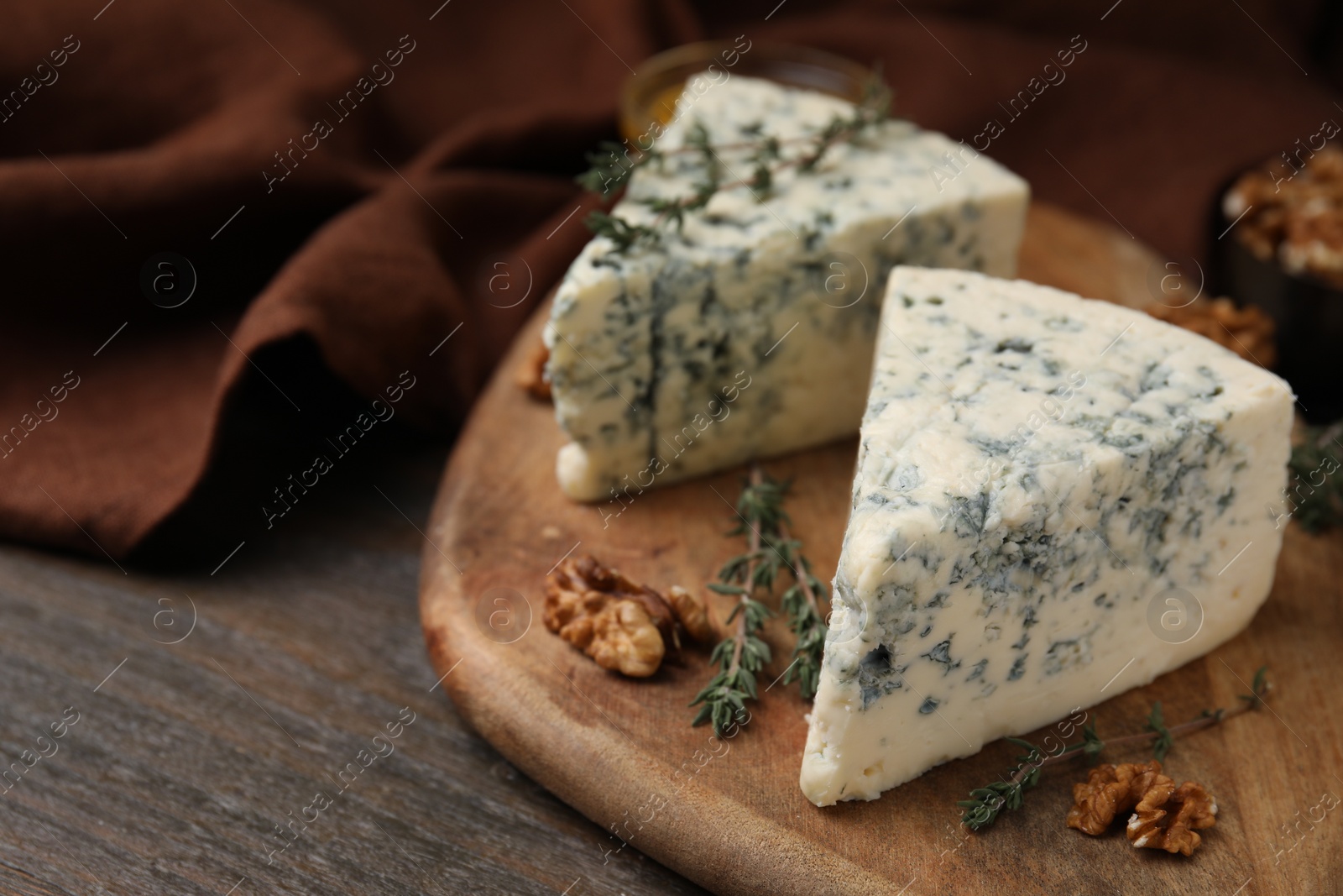 Photo of Tasty blue cheese with thyme and walnuts on wooden table, closeup. Space for text