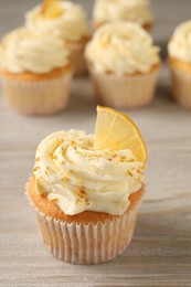 Photo of Tasty cupcake with cream, zest and lemon slice on light wooden table, closeup