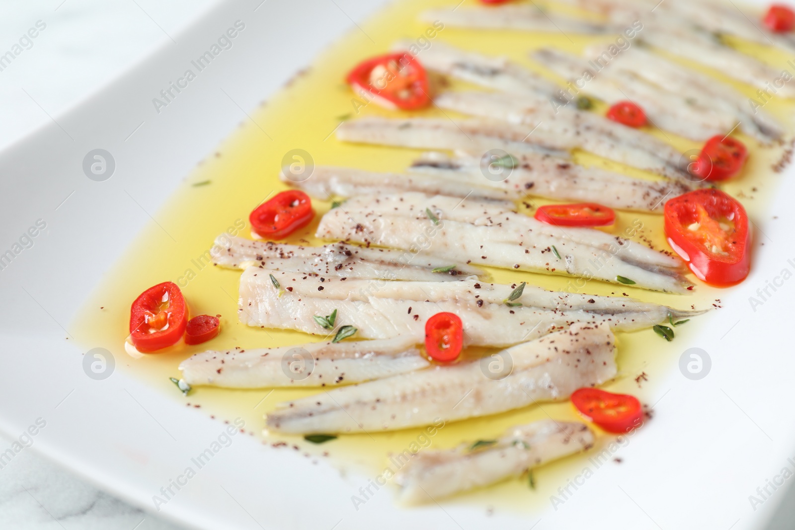 Photo of Tasty pickled anchovies with spices on plate, closeup