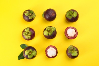 Photo of Fresh ripe mangosteen fruits with green leaves on yellow background, flat lay