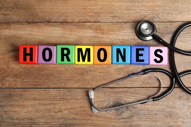 Photo of Word Hormones made of colorful cubes with letters and stethoscope on wooden background, flat lay