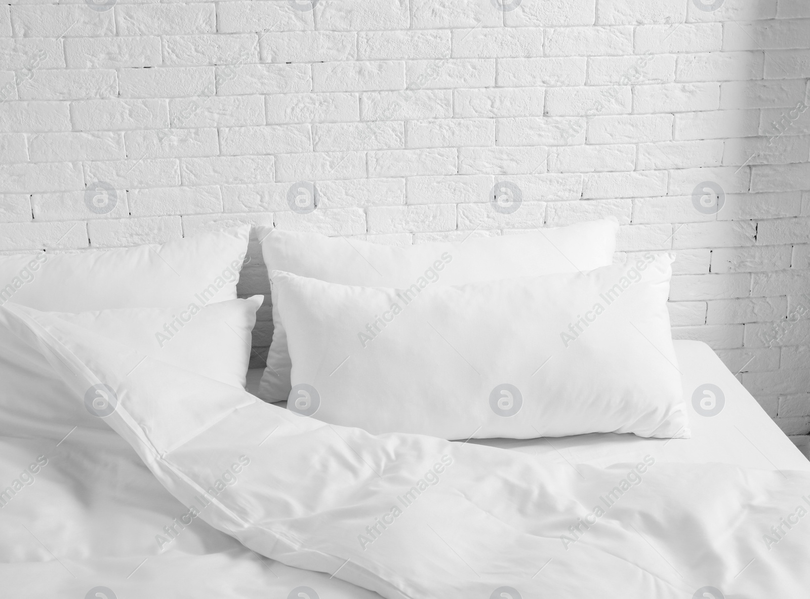 Photo of Large comfortable bed with pillows and blanket near white brick wall indoors. Stylish interior