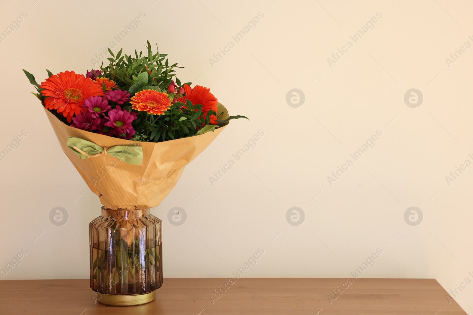 Photo of Bouquet of flowers on wooden table near white wall. Space for text