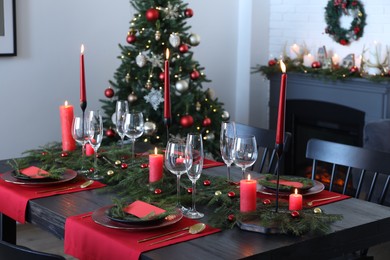 Photo of Elegant Christmas table setting with dishware and burning candles in festively decorated room