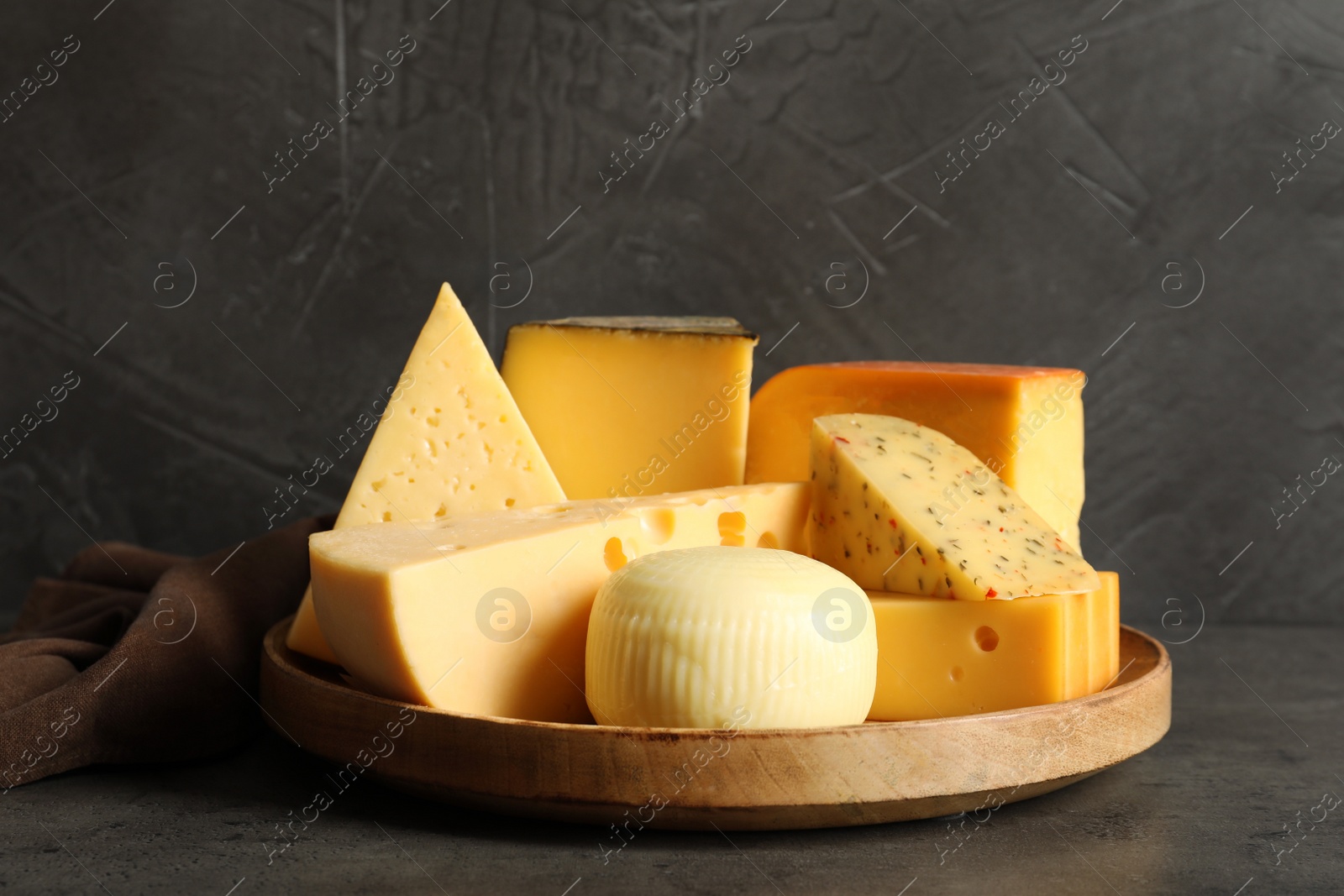 Photo of Wooden plate with different sorts of cheese on grey table