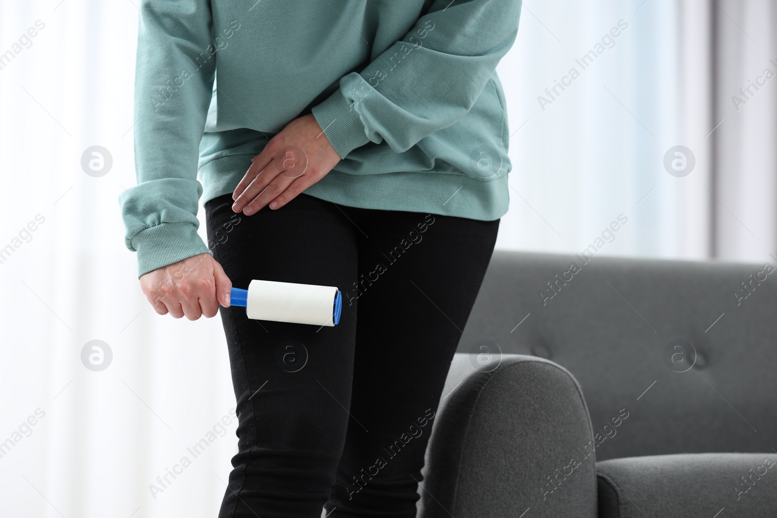 Photo of Woman with lint roller removing pet hair from black trousers indoors, closeup