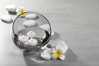 Photo of Vase of water with burning candles and spa stones on grey table, space for text